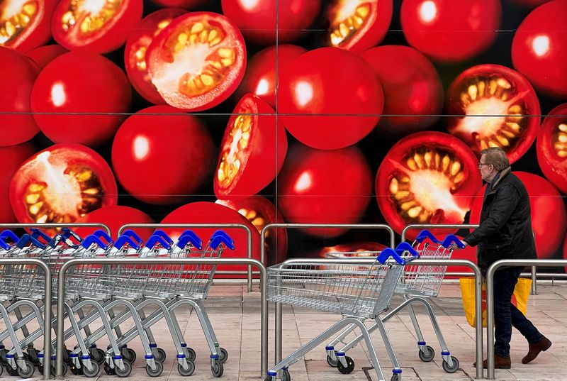 © Reuters. FILE PHOTO: A shopper walks next to a photographic depiction of tomatoes on a Tesco supermarket as Britain experiences a seasonal shortage of some fruit and vegetables, in London, Britain, February 26, 2023. REUTERS/Toby Melville/File Photo