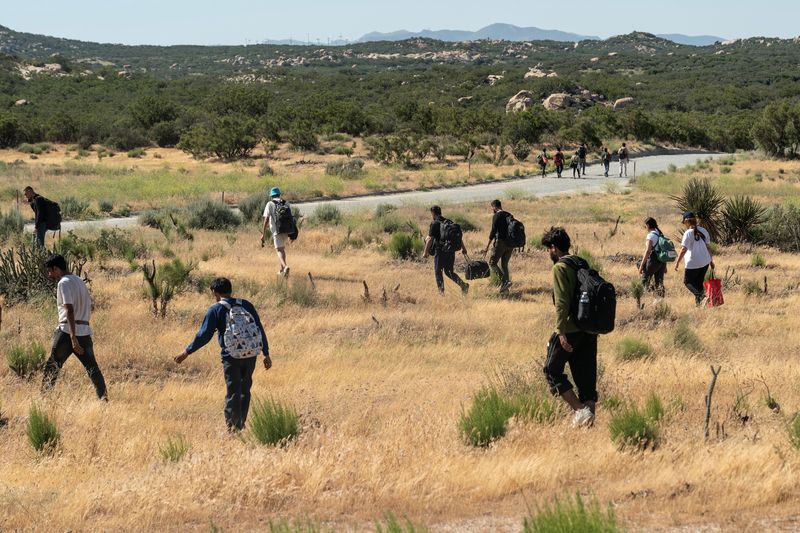 © Reuters. Asylum-seeking migrants walk near the border to leave a temporary staging area to be transported, after U.S. President Joe Biden announced a sweeping border security enforcement effort, in Jacumba Hot Springs, California, U.S. June 4, 2024.  REUTERS/Go Nakamura