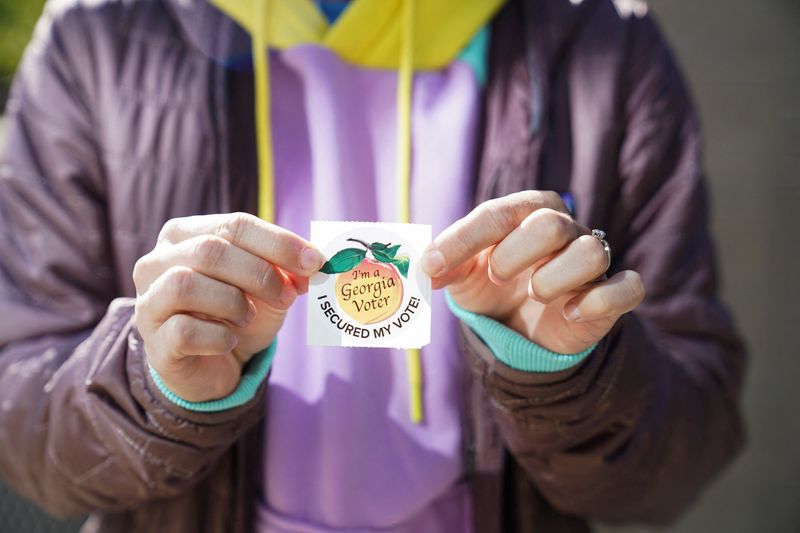 © Reuters. FILE PHOTO: A person holds a sticker after voting, as voters attend a polling station, as Georgians turned out a day after the battleground state opened early voting, in Atlanta, Georgia, U.S., October 16, 2024. REUTERS/Megan Varner/File Photo