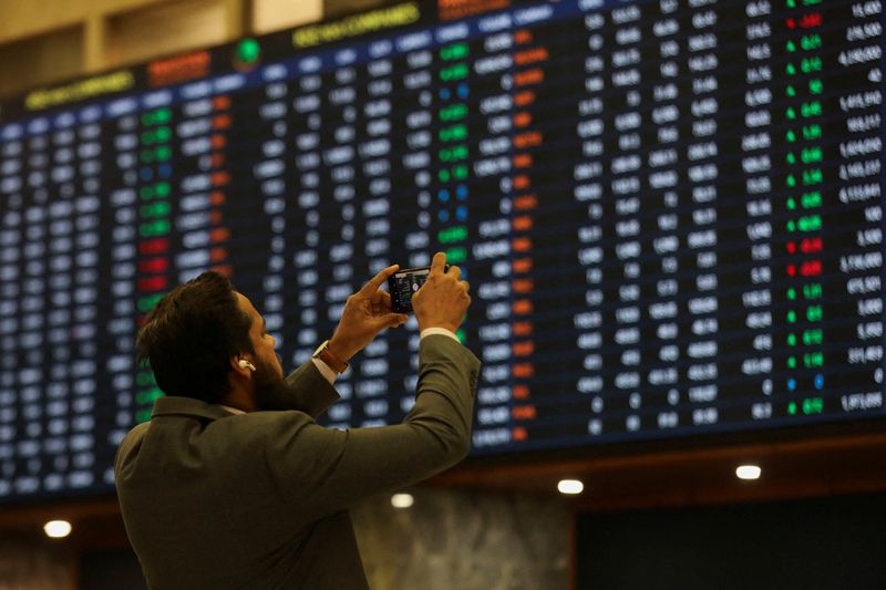 © Reuters. FILE PHOTO: A man uses a mobile phone as he takes a photo of the electronic board displaying share prices during a trading session at the Pakistan Stock Exchange, in Karachi, Pakistan November 28, 2023. REUTERS/Akhtar Soomro/File Photo